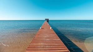 Kirkkaan taivaan alla tyyniin, siniseen veteen ulottuva puinen laituri.