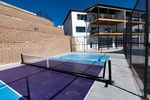 A tennis court with a net, adjacent to a building with balconies and a brick wall. - Unique Lakeview Home with Indoor Pool in Basement! (Branson)