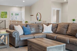 A modern living room with a sectional sofa, a wooden coffee table, and a dining area with chairs and a table. - Unique Lakeview Home with Indoor Pool in Basement! (Branson)