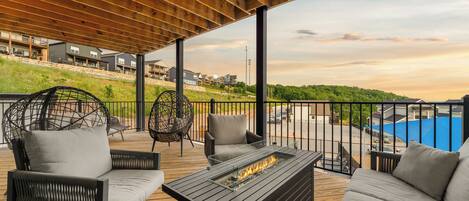A covered outdoor deck with seating, a fire feature, and a view of a residential area.