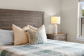 A bedroom with a bed, pillows, a bedside table with a lamp, and a window. - Unique Lakeview Home with Indoor Pool in Basement! (Branson)