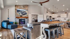 A modern living room with a fireplace, a television, and a dining area with bar stools. - Unique Lakeview Home with Indoor Pool in Basement! (Branson)