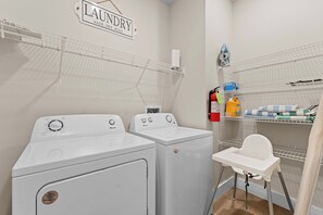 A laundry room with two white Amana washers, a drying rack, a folding station, and shelves with laundry supplies. - Unique Lakeview Home with Indoor Pool in Basement! (Branson)