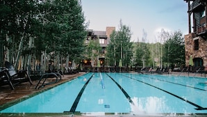 Ein Swimmingpool mit Liegestühlen und Sonnenschirmen, umgeben von Bäumen und Gebäuden aus Stein.