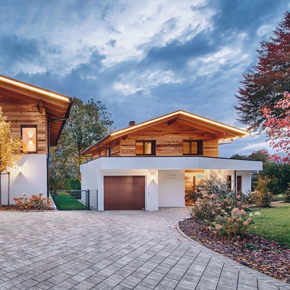 A modern two-story house with a garage, wooden exterior, and a paved driveway.