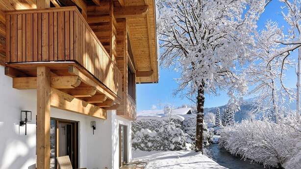 Una cabaña de madera con balcón, un sendero de piedra y alrededores cubiertos de nieve.