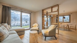 Un salón amplio con un gran ventanal, un sofá, una mesa redonda de madera y una zona de comedor con mesa y sillas.
