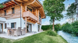 Una casa de madera de dos pisos con un balcón, un patio con muebles de exterior y un río al fondo.