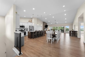 A spacious kitchen with modern appliances, a dining area with wooden chairs, and large windows offering a view.