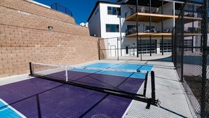 A tennis court with a net, adjacent to a building with balconies and a brick wall.