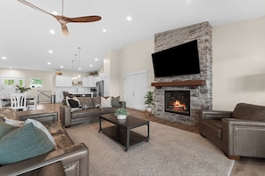 A spacious living area with a fireplace, leather sofas, a coffee table, and a television mounted on a stone wall.