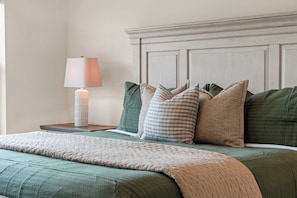 A neatly made bed with a green quilt, a white lamp on a bedside table, and a headboard with a panel design.