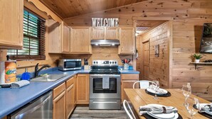 A wooden cabin-style kitchen with a stainless steel stove, a microwave, and wooden cabinets.