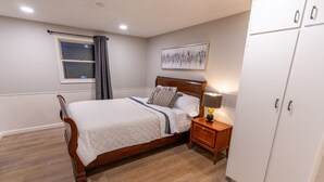 Un dormitorio con cama de madera, una mesita de noche con lámpara, un armario y una ventana con cortinas.