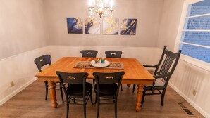 Comedor con mesa de madera, sillas negras, candelabro y obras de arte azules y doradas en la pared.