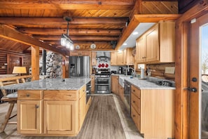 A log cabin kitchen with wooden cabinets, granite countertops, a central island, and a stone wall.