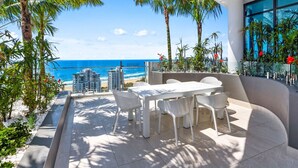 Eine moderne Außenpatio mit einem weißen Tisch und Stühlen, umgeben von Palmen und Blick aufs Meer.