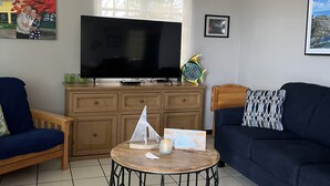 A living room with a TV, a wooden cabinet, a blue sofa, a round coffee table, and a painting on the wall.
