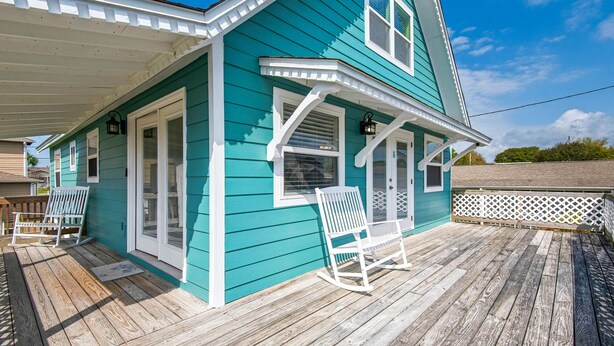 A turquoise house with a wooden deck, two rocking chairs, and a covered porch.