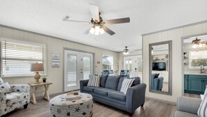 A living room with a blue sofa, round ottoman, and a ceiling fan.