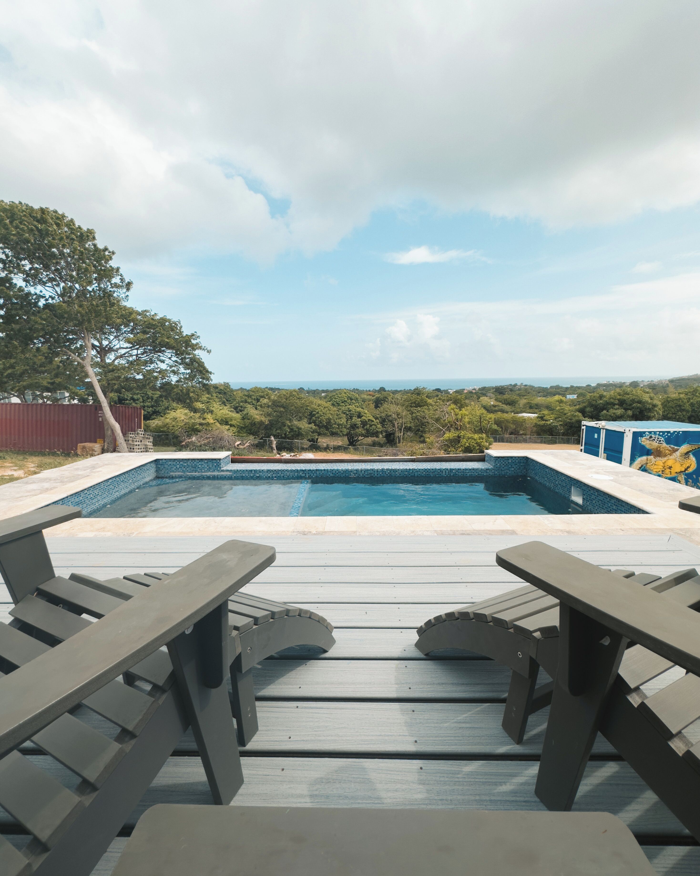Una piscina con vistas al paisaje, rodeada de una terraza de madera y mesas de picnic.