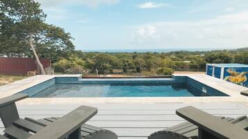 Una piscina con vistas al paisaje, rodeada de una terraza de madera y mesas de picnic.