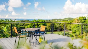 A deck with a table and chairs, overlooking a lush landscape and the sea. - Tiny house on an acre with ocean view and private infinity pool.  (Vieques)