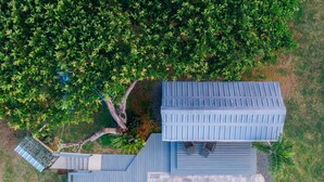An aerial view of a property with a swimming pool, a deck area with seating, and lush greenery surrounding the buildings. - Tiny house on an acre with ocean view and private infinity pool.  (Vieques)
