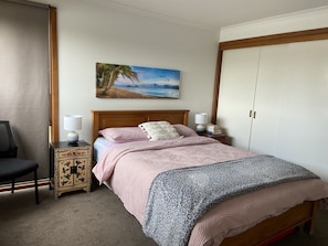 Una camera da letto con un letto, due comodini, una sedia, un quadro e un armadio.