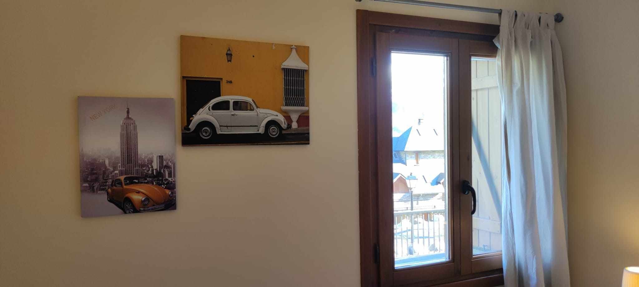 Une pièce avec une porte donnant sur un espace extérieur, un mur orné de deux tableaux encadrés et une fenêtre avec des rideaux.
