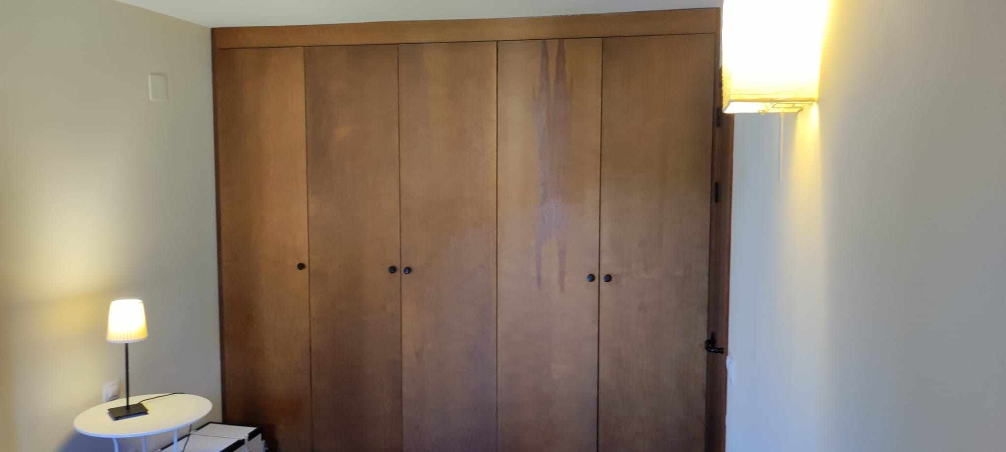 Une grande armoire en bois à deux portes et une petite table avec une lampe placée à côté.