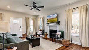 Una sala de estar con chimenea, ventilador de techo y televisor en la pared.