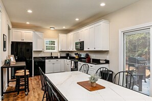 A modern kitchen with white cabinets, a black refrigerator, and a dining area with a marble countertop and wooden stools. - The 19th Hole - Poker Table - 2 mins to Pinehurst (Pinehurst)