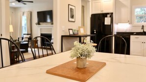 Una cocina moderna con gabinetes blancos, un refrigerador negro y un comedor con mesa y sillas.