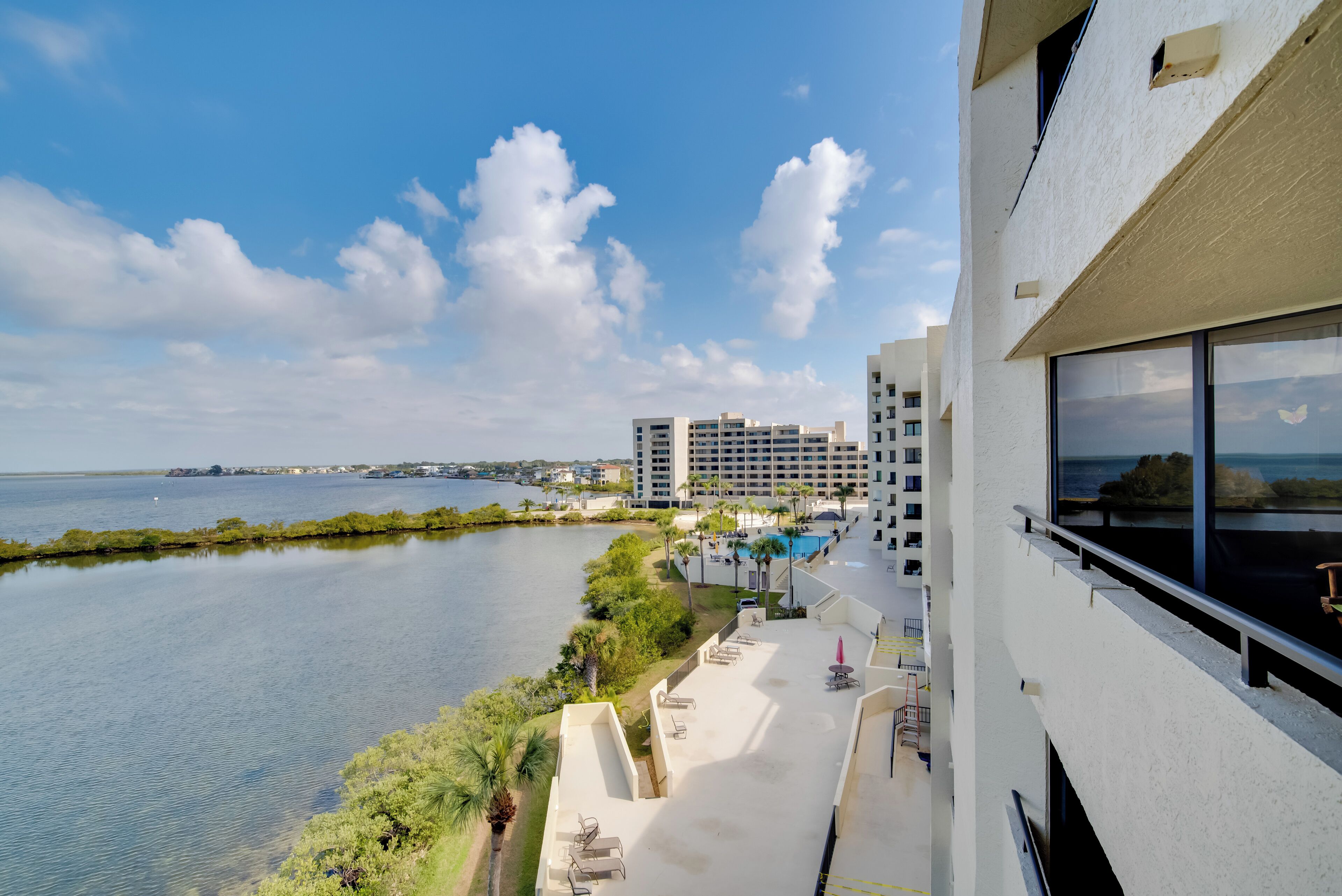 A high-rise hotel with a view of a calm body of water, a pool area, and a clear sky.