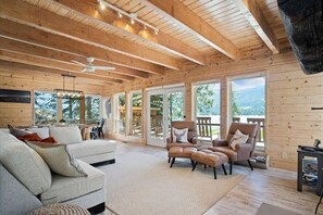 A spacious cabin with a high ceiling, wooden beams, a large sofa, two armchairs, and a dining area. - New! Modern Cabin w/fireplace/hot tub/sleeps 12 (Donnelly)