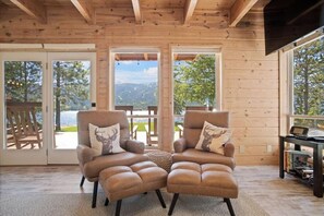 A cozy cabin interior with two leather armchairs facing a large window overlooking a scenic outdoor area. - New! Modern Cabin w/fireplace/hot tub/sleeps 12 (Donnelly)