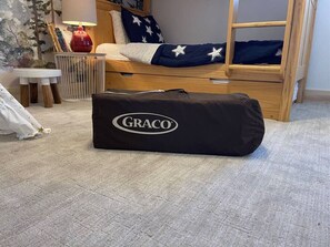 A bunk bed with a star-patterned pillow, a red lamp, and a GRACO bag on the floor.