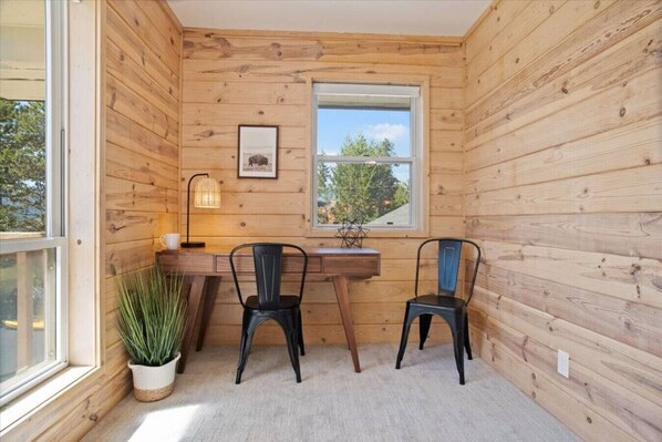 A room with wooden walls, a desk, two chairs, a potted plant, a window, and a framed picture.