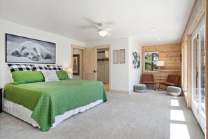A bedroom with a large bed, a ceiling fan, and a window with a view of trees.