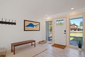 A modern interior with a wooden bench, a map on the wall, and a view of a house through the door.