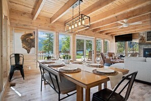 A spacious dining area with a wooden table set for four, large windows offering a view of the outdoors, and a cozy seating area with a fireplace.