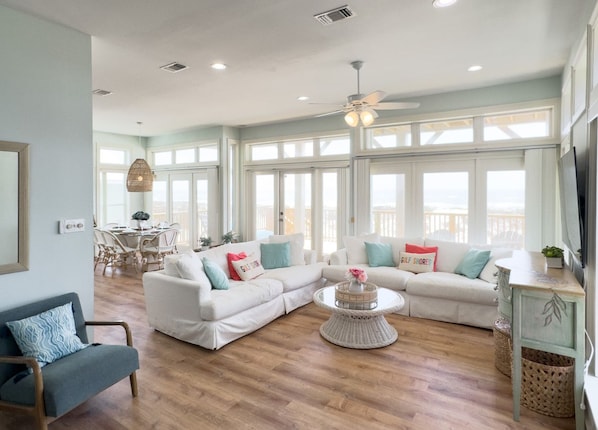 A spacious living room with a large window, a ceiling fan, and a dining area with a table and chairs.