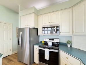 A kitchen with white cabinetry, a stainless steel refrigerator, a stove, and a microwave.