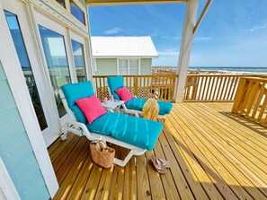 Una terraza de madera con dos sillones de descanso, uno con cojín azul y otro con cojín rosa.