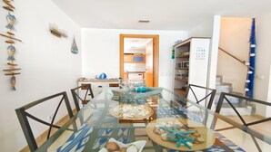 Un comedor con mesa de vidrio, sillas y vistas a la cocina y la escalera.