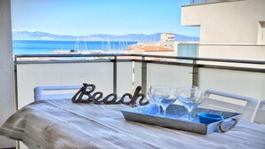 Un balcón con una mesa preparada para bebidas, un letrero que dice "Beach" y vista al mar y edificios.