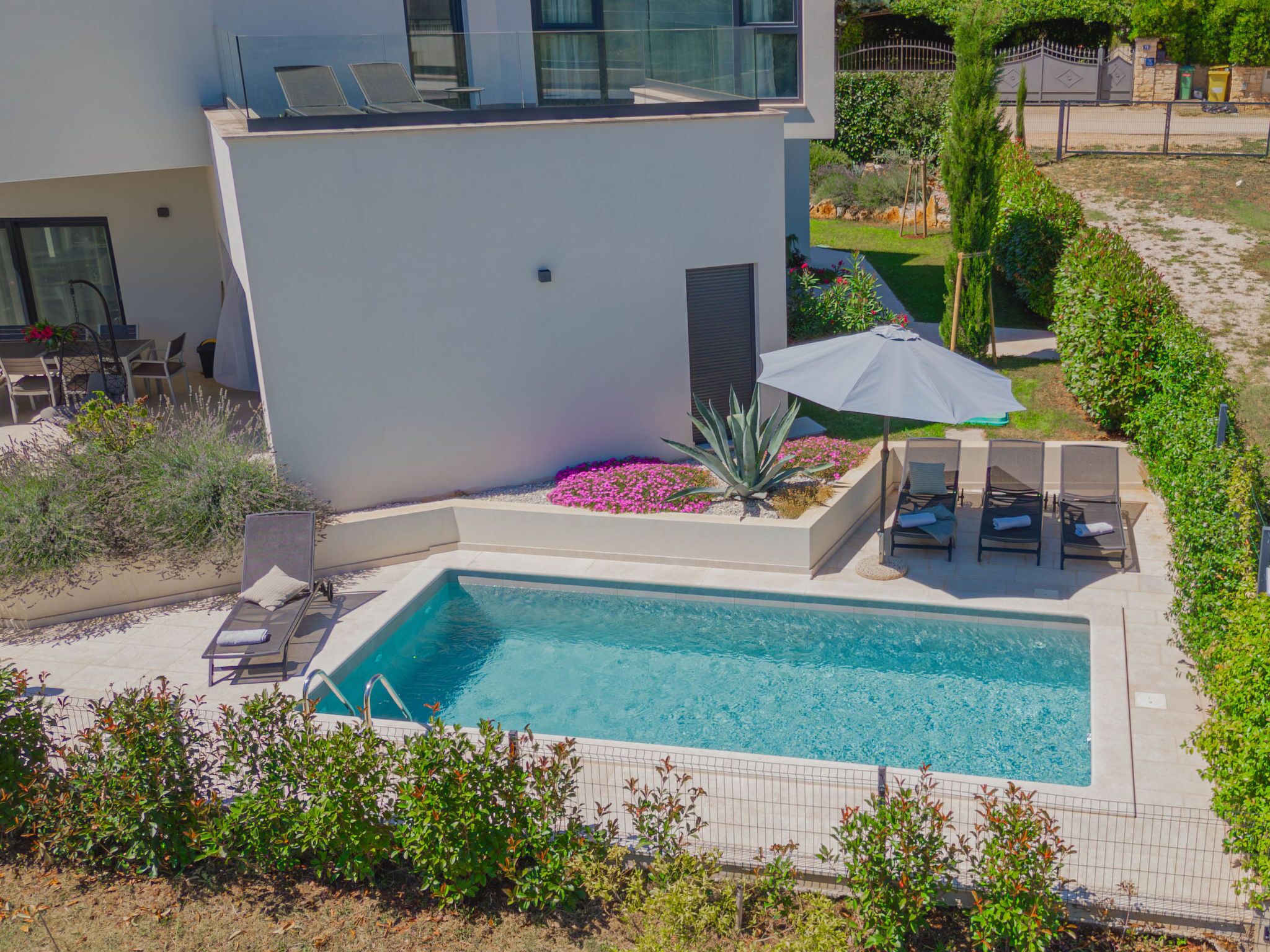 A modern pool area with a rectangular pool, lounge chairs, and a pergola with an umbrella.