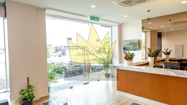 A hotel reception area with a modern design, including a reception desk, seating area, and a large window with a view of the street. - The Crown Hotel Klia (Sepang)