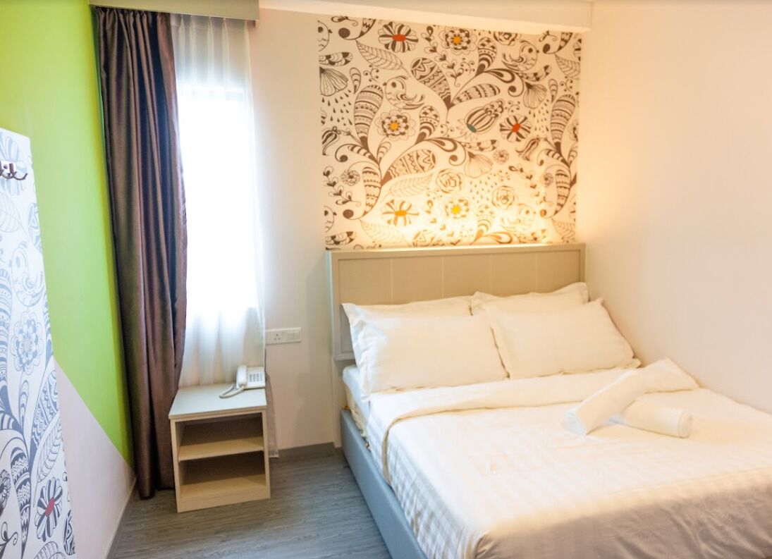 A hotel room with a bed, a bedside table, a telephone, and a window with curtains.